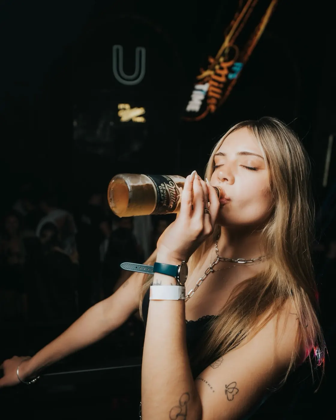 Chica tomando una cerveza bajo el neón de la U