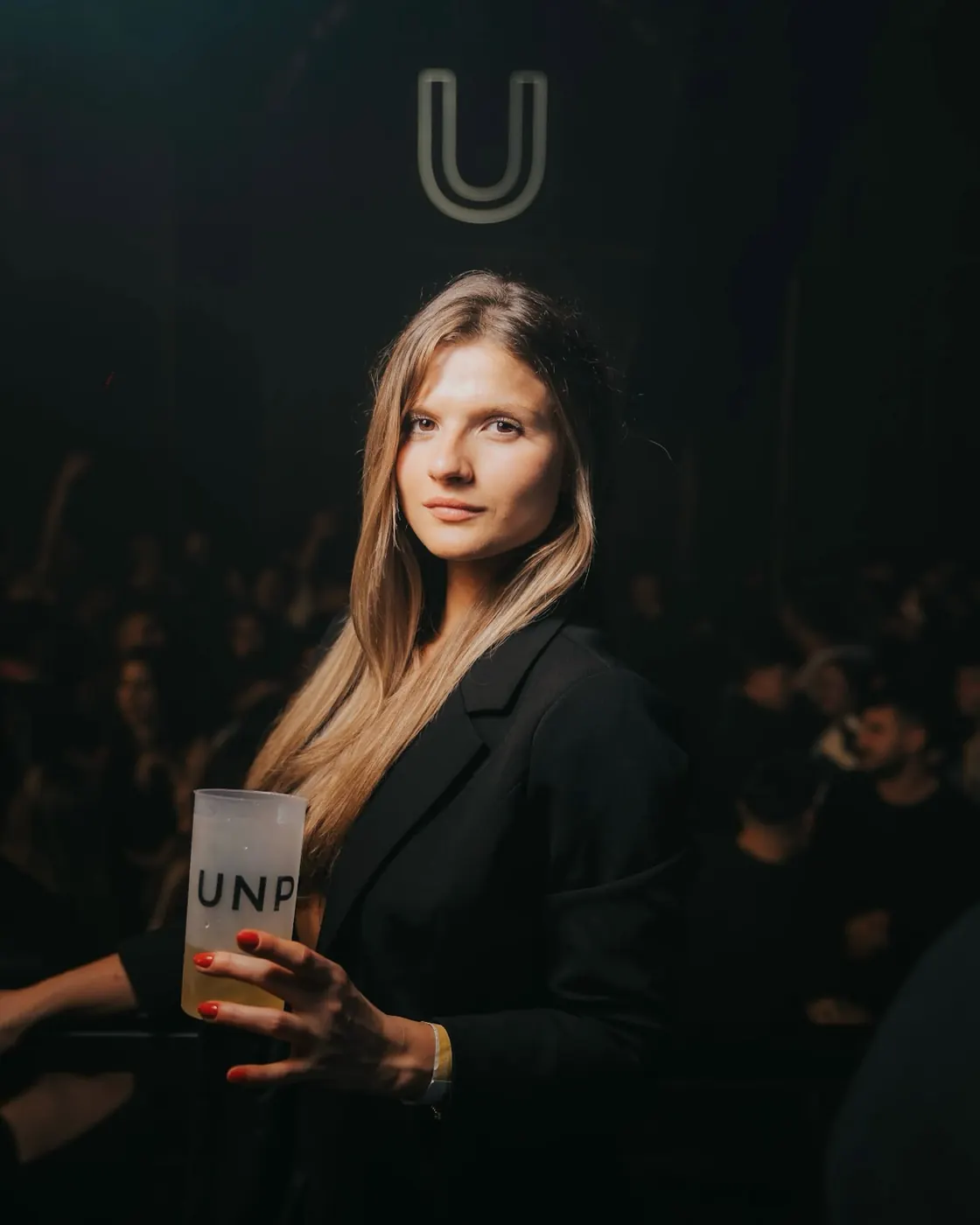 Chica con vaso UNP bajo el neón de la U